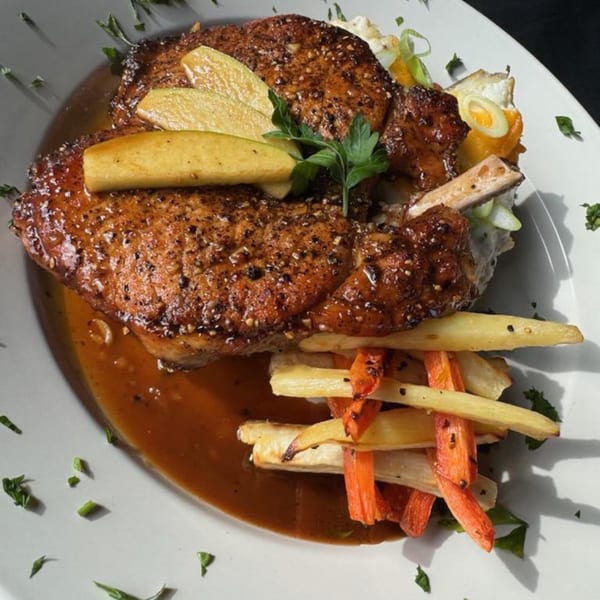 Two bone-in pork chops with apples, parsnips, carrots, and gravy on a white plate.