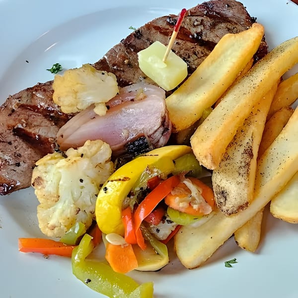 Grilled steak, fries, roasted cauliflower, and mixed vegetables with a butter pat on a white plate.
